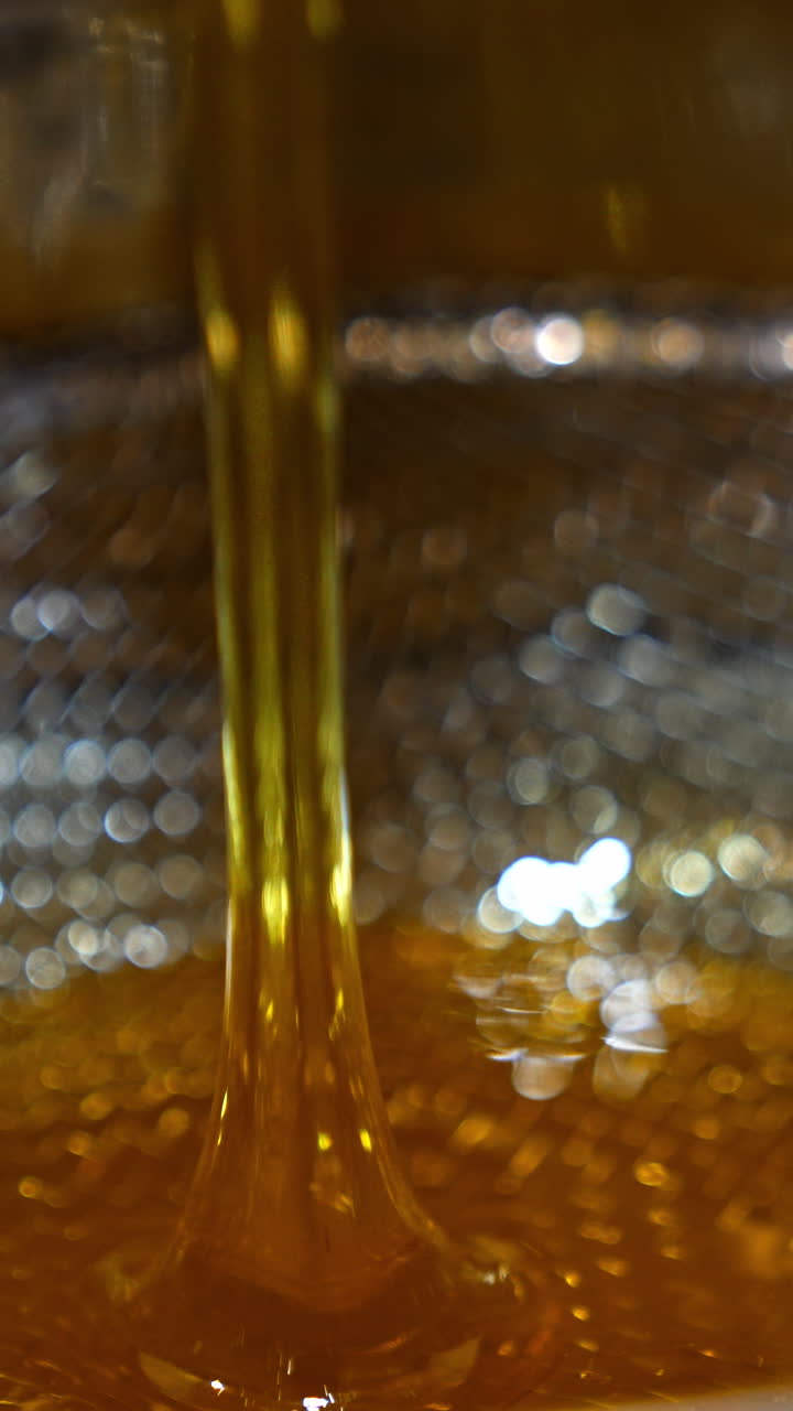 Little stream of honey flowing onto the metal sieve. Close up. Organic honey filtering after being extracted from frames. Vertical video