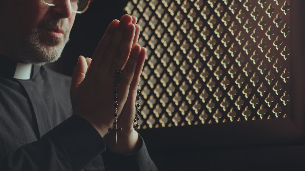Priest Holding Rosaries and Saying Prayer in Confessional Booth
