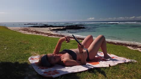 A-shot-of-a-woman-reading-in-a-ebook-on-the-beach-in-a-beautiful-place,-in-Mauritius