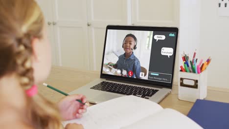 Schoolgirl-using-laptop-for-online-lesson-at-home,-with-her-colleague-and-web-chat-on-screen