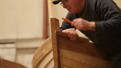 experienced carpenter marking boat bow of traditional wooden boat.