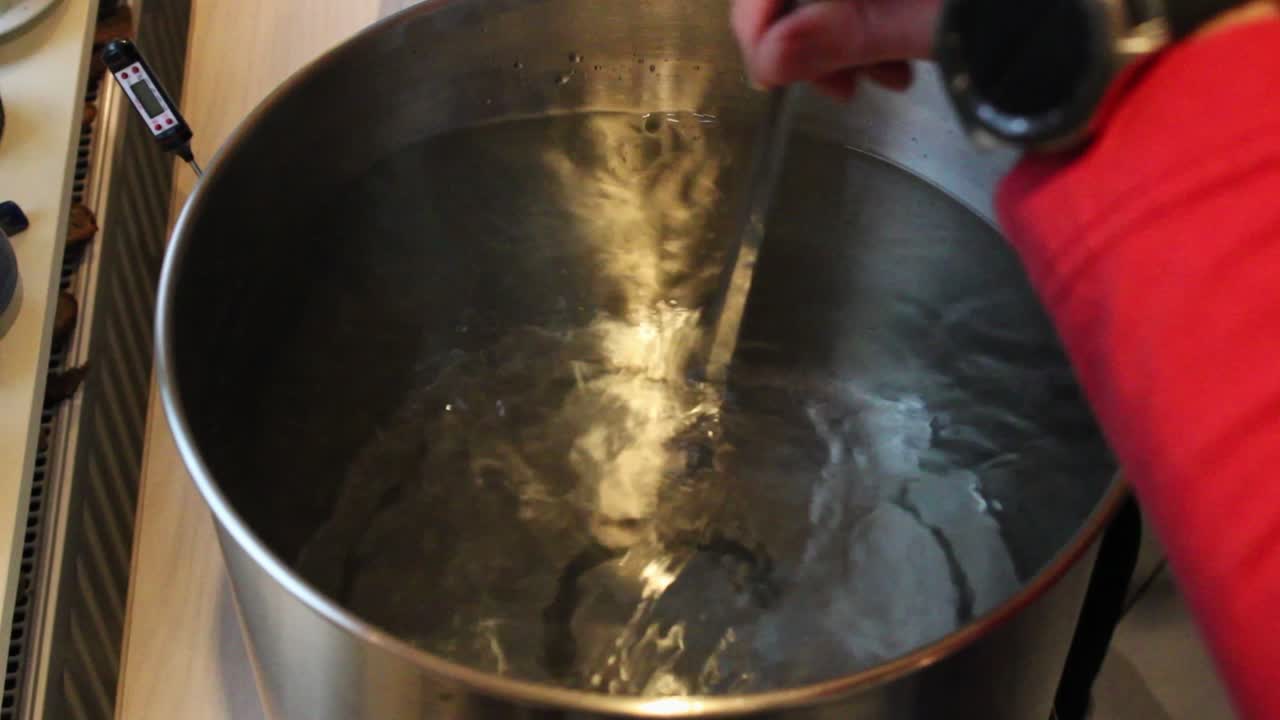 Mani di un uomo che mescolano malto d'orzo in una caldaia d'acciaio riempita con acqua calda
