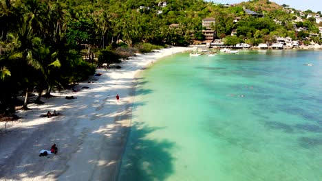 a slow aerial drone shot approach of shark bay, showing its white sandy beach, crystal blue waters, and with tourists relaxing at the beachfront in the island of koh tao, surat thani, thailand