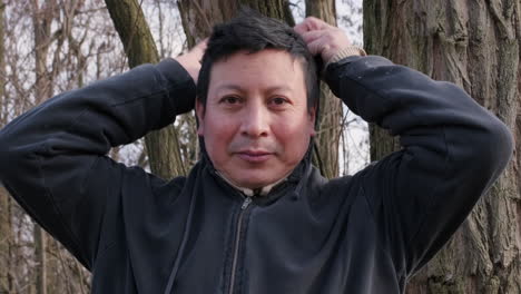 happy ecuadorian man puts his sweatshirt hood during an outdoor walk at sunny winter afternoon in forest park