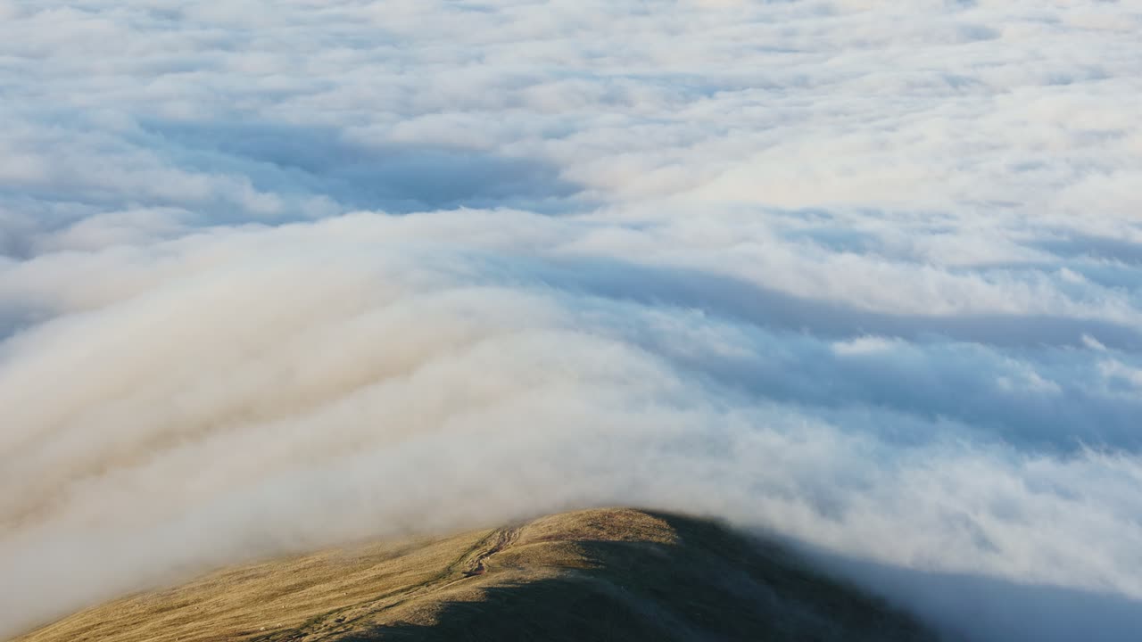 Static shot of a temperature inversion with clouds flowing over a mountain ridge