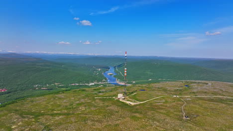 Toma-Aérea-De-Seguimiento-De-Una-Torre-De-Radio-En-La-Cima-De-Una-Montaña-En-La-Soleada-Utsjoki,-Finlandia.