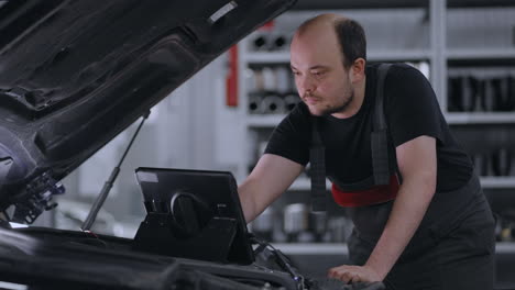 male mechanic uses a tablet computer with an augmented reality diagnostics software. specialist inspecting the car in order to find broken components inside the engine bay. modern car service.