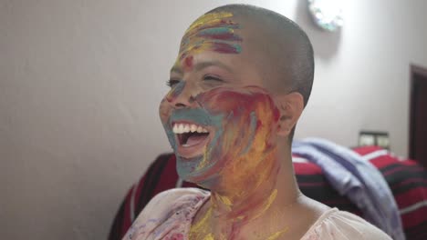 happy and hopeful cancer patient bald girl applies colored powder on cheeks at home on holi and laughs