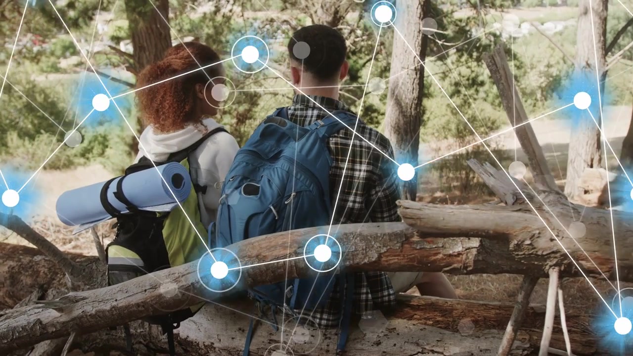 Coppia di escursionisti con gli zaini che riposa su un tronco, guardando verso una radura mentre nodi tecnologici si sovrappongono e crescono