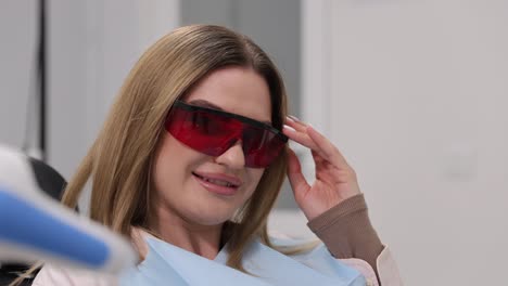 a cheerful woman is at the dentists office, wearing protective eyewear and smiling confidently throughout her visit