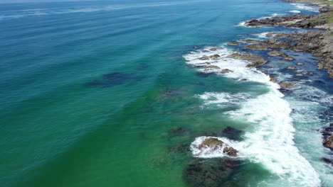 aerial shot looking along the west coastline of scotland, with a turquoise sea and waves crashing on rocks=
