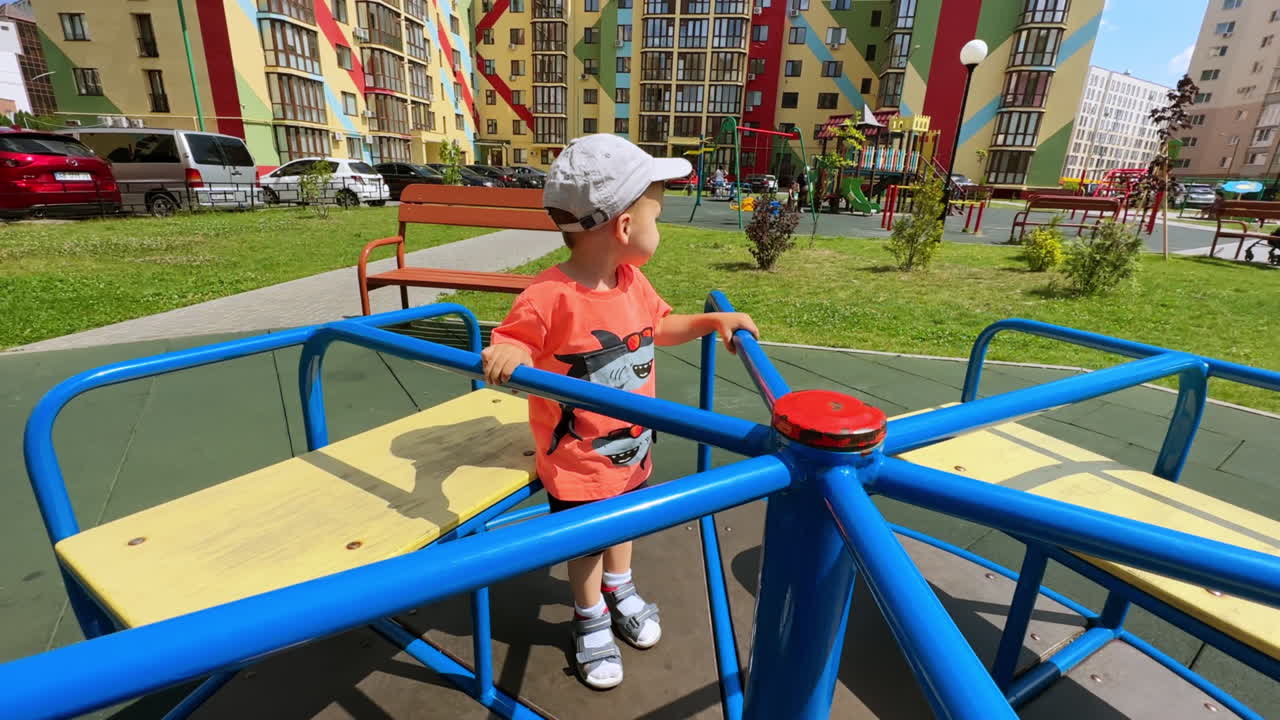 Little kid stands on the merry-go-round. Adorable toddler on the playground in the yard.