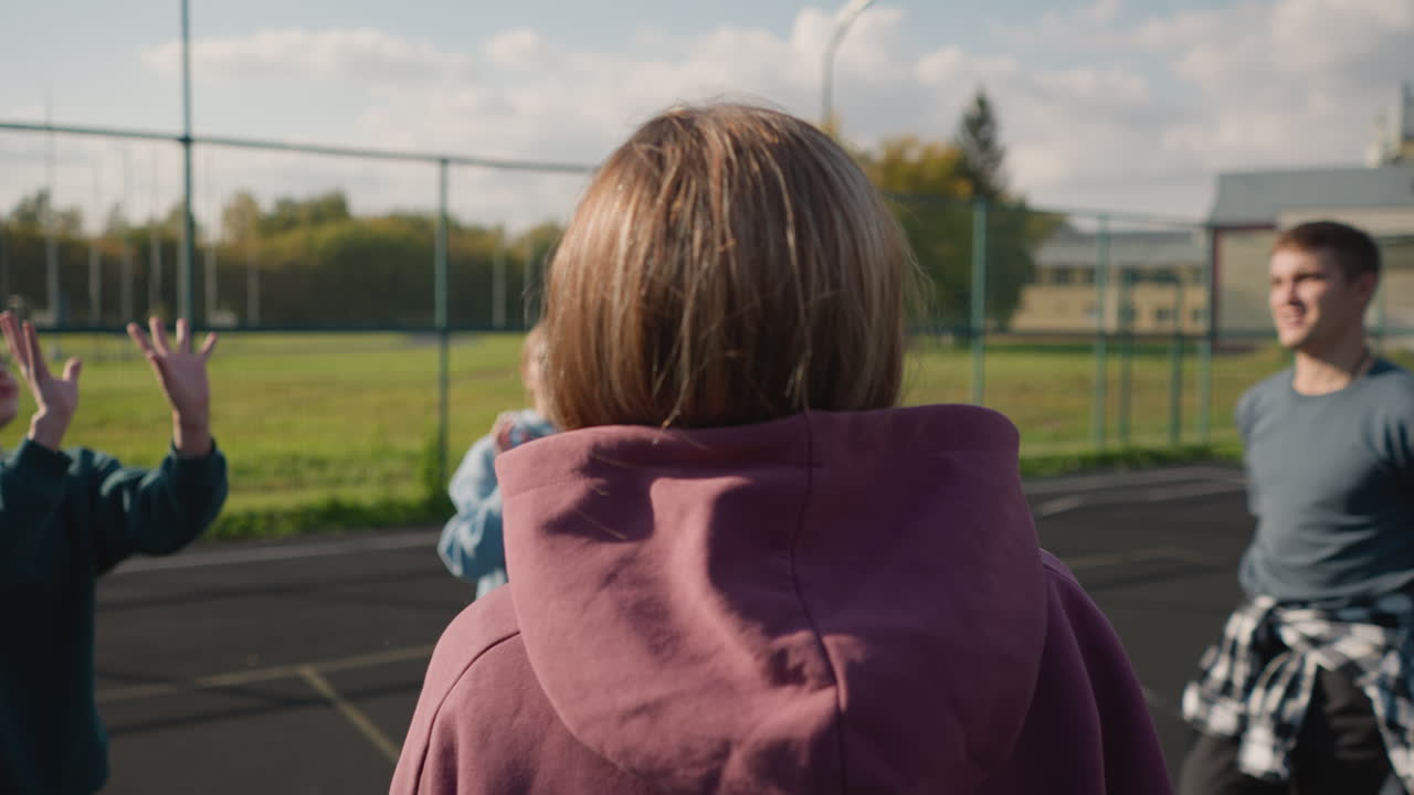 배경에는 바 울타리와 초록색으로 열린 코트에서 볼리볼을 연습하는 후디를 입은 여자의 뒷면, 이 많은 야외 스포츠 환경에서 개별 연습 기술에 초점을 맞추십시오.
