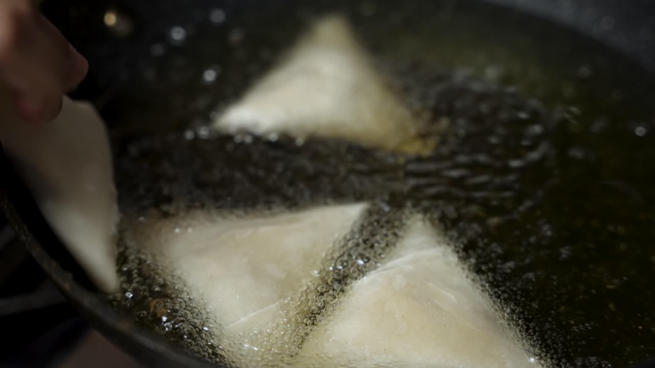 Close up view of samosas frying in hot oil, bubbling and sizzling, creating a tempting scene of crispy, golden brown perfection