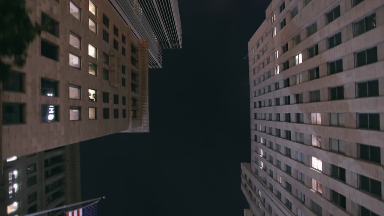 LA: Downtown LA skyscrapers looking up from the sunroof of a car at night with lens flare and American flag - Los Angeles California, USA