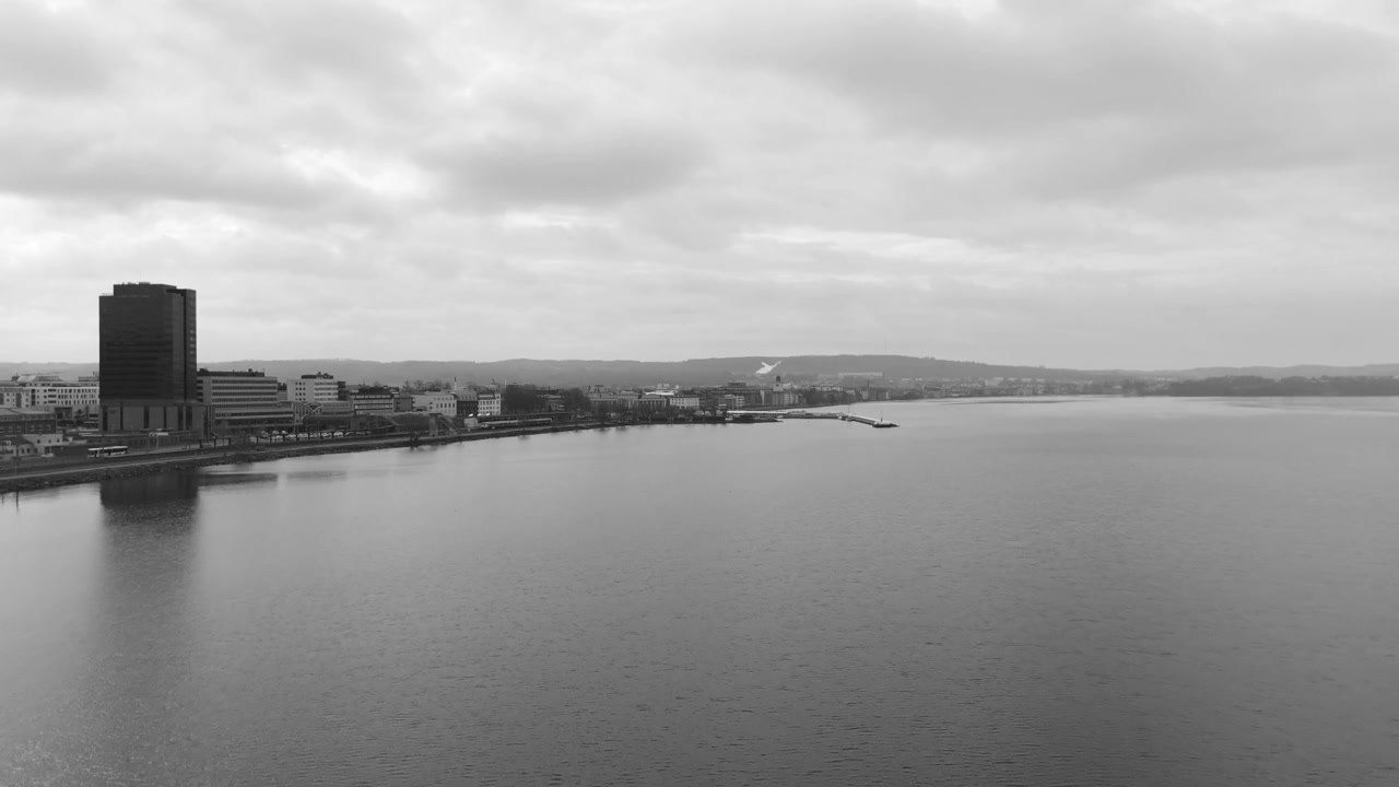 Black and white aerial drone shot of Jonkoping showing city skyline along Lake Vattern with calm water and cloudy sky creating minimal urban waterfront scene