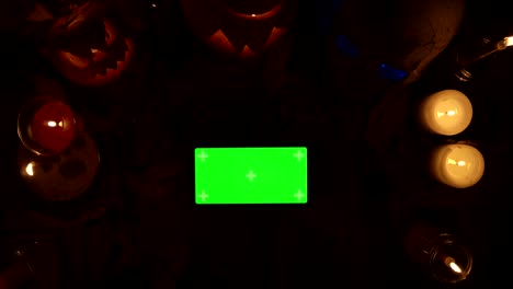usando un teléfono inteligente con pantalla verde en el fondo de la decoración de halloween por la noche