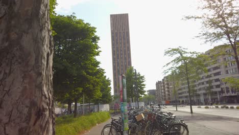 bicycle parking on the sidewalk in the city of eindhoven with tall hotel building in background