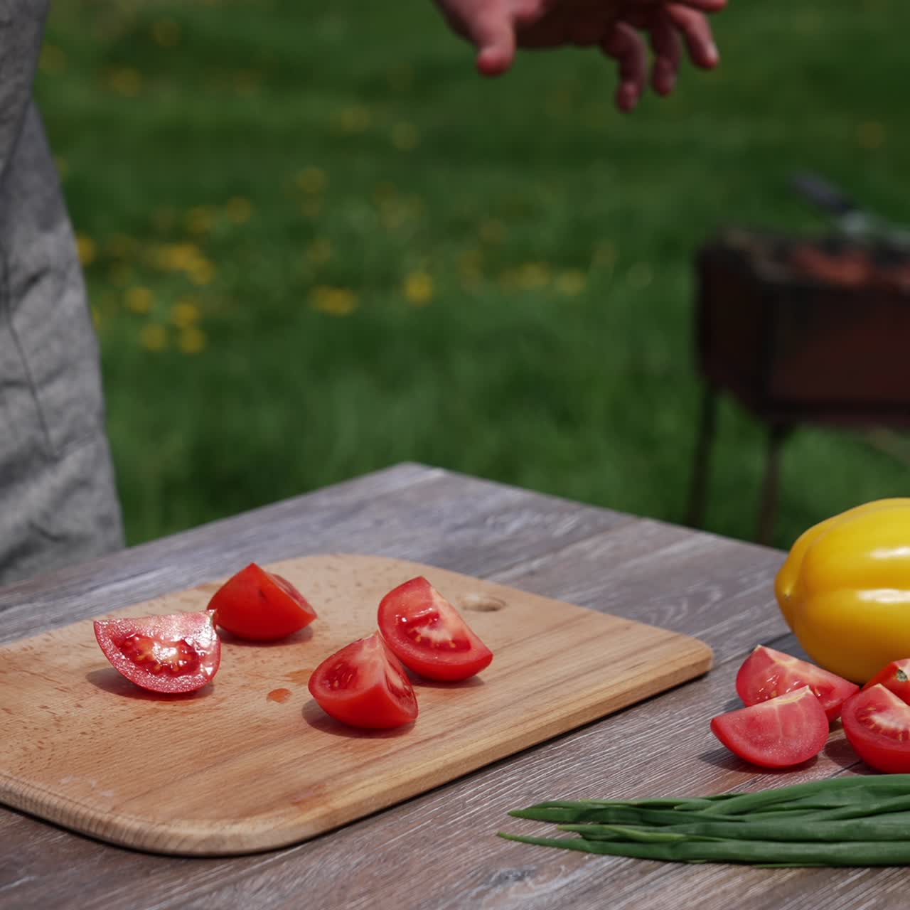 Man cutting tomato on a board outdoors. Preparing dinner at dacha. Man cuts vegetable into four parts on a table before the picnic