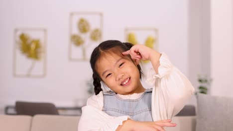 young asian girl with pigtails performs playful thinking gestures and expressions in a bright, modern living room with soft, even lighting and static camera