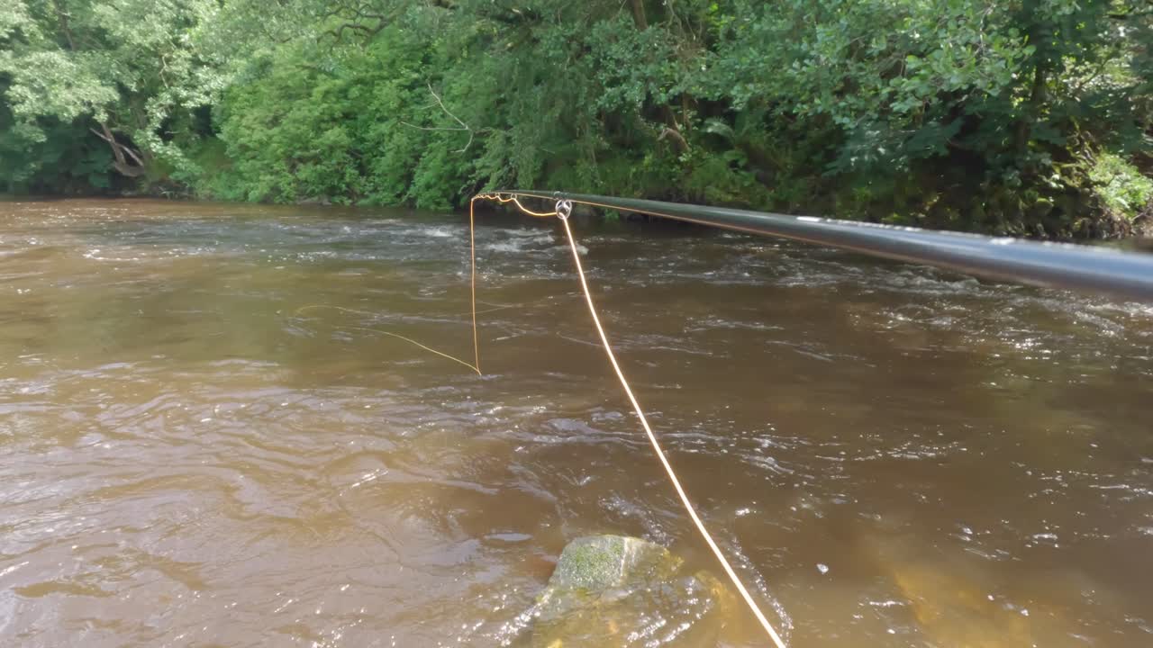 pov disparó siguiendo una caña de pescar mosca y línea por un río marrón turbio