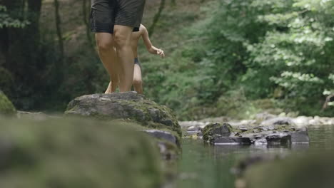 people walking across rocks in a forest river