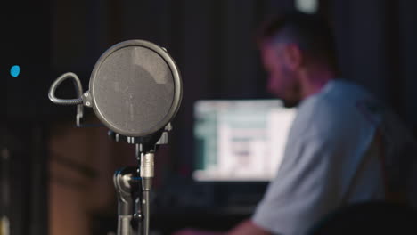 a man sitting in front of a computer in a home recording studio with a professional microphone.