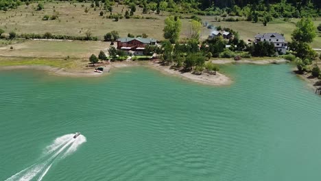 jet skiing on a green water lake with a wooden house on the edge of it