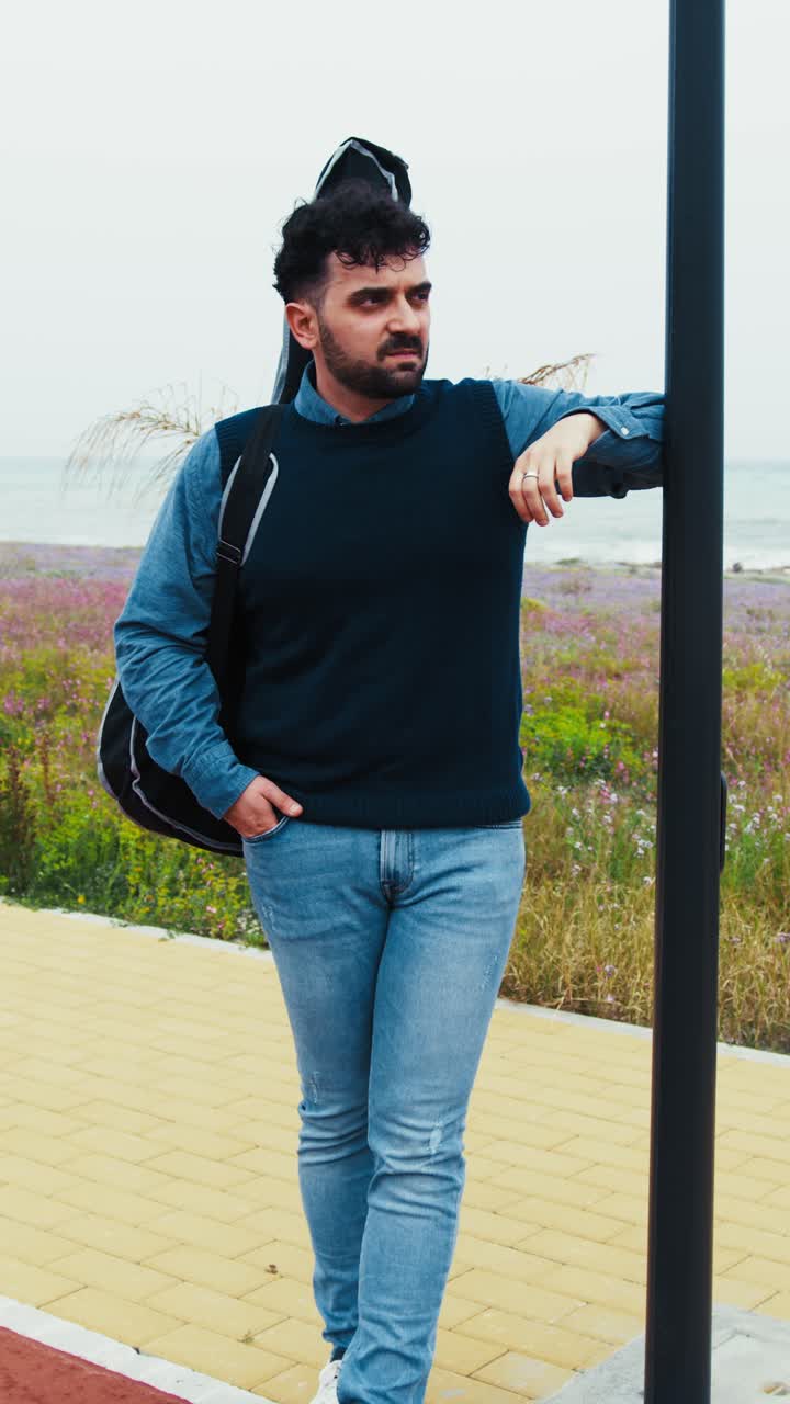 Musician With Guitar on Back Waits for Someone to Pick Him Up