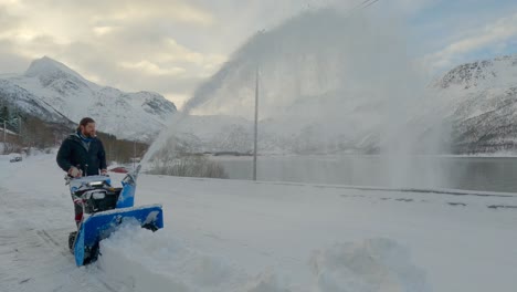 Young-male-clearing-the-driveway-with-a-snow-blower,-throwing-snow-far-across-the-road-on-the-other-side,-static-shot