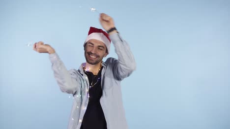 Happy-New-Year-Cheerful-young-caucasian-man-in-casual-clothes-and-santa-hat-holding-two-sparklers,-waving-them-in-a-rhythm-and