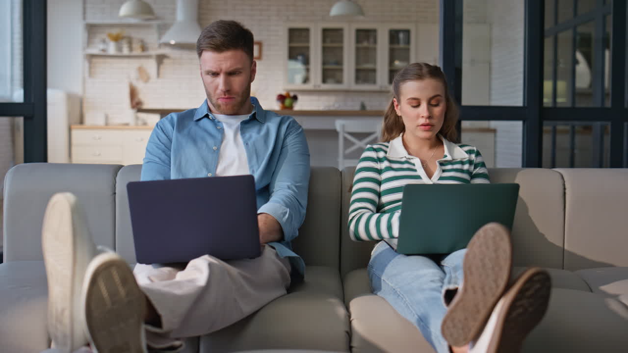 Involved freelancers working computers at sofa together. Focused husband wife