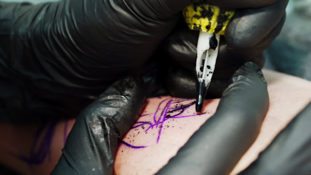 Ink machine splashes black paint while working. Tattoo artist stretching the skin for better performance. Close up.