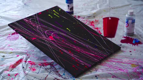 paint in a cup swings over a black canvas, spreading bright neon paint over it