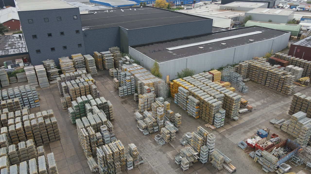 Aerial view of an industrial storage yard with high stacks of construction materials. A forklift truck drives around while a truck is being loaded with cargo