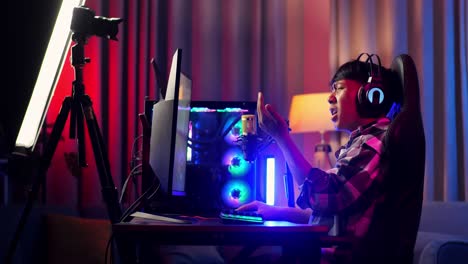 side view of asian boy streamer playing game over network on personal computer. challenge and bully threat killing competitor, live stream video game, desk illuminated by rgb led strip light