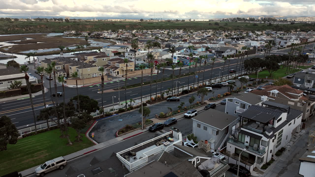 Droneoptagelser af huse ved stranden i Newport Beach, Californien, i regnvejr. Den overskyede himmel og fugtige kystlinje står i kontrast til det strukturerede layout af kystens boligejendomme.