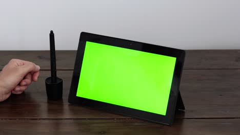 tablet with a green screen, electronic signature with a hand. on a wooden table.