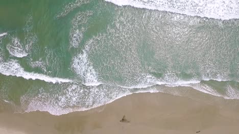 birds eye view of a light blue sea breaking in a sandy beach