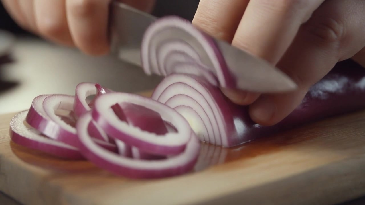 Chef che affetta cipolla rossa fresca su un tagliere di legno