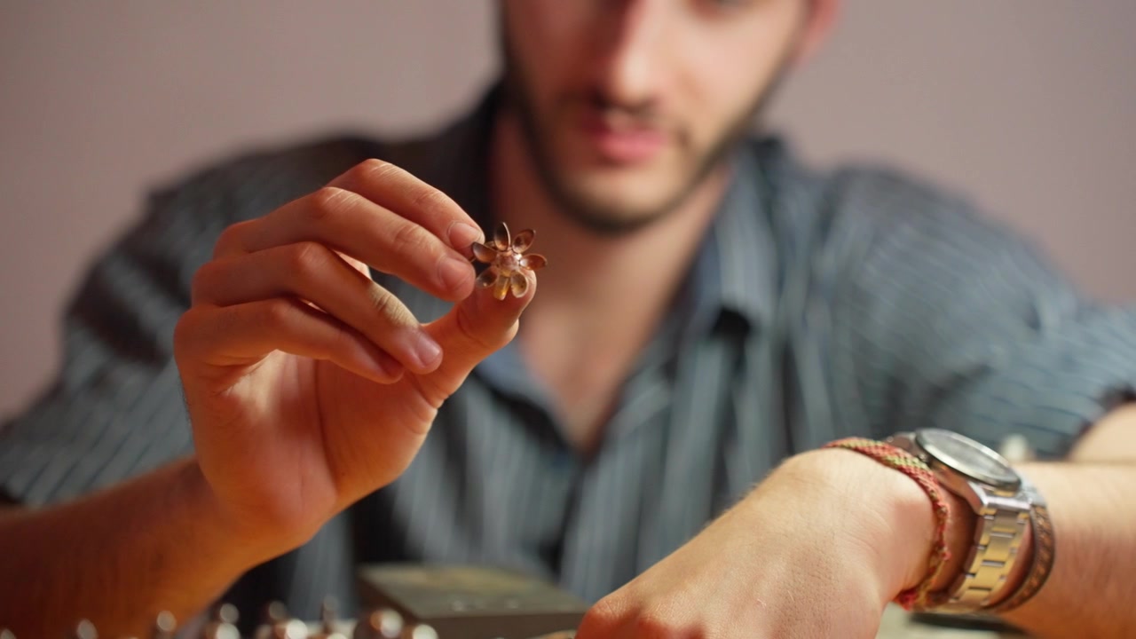 A person intently examines a small model piece in a well-lit workspace, surrounded by various tools and components.
