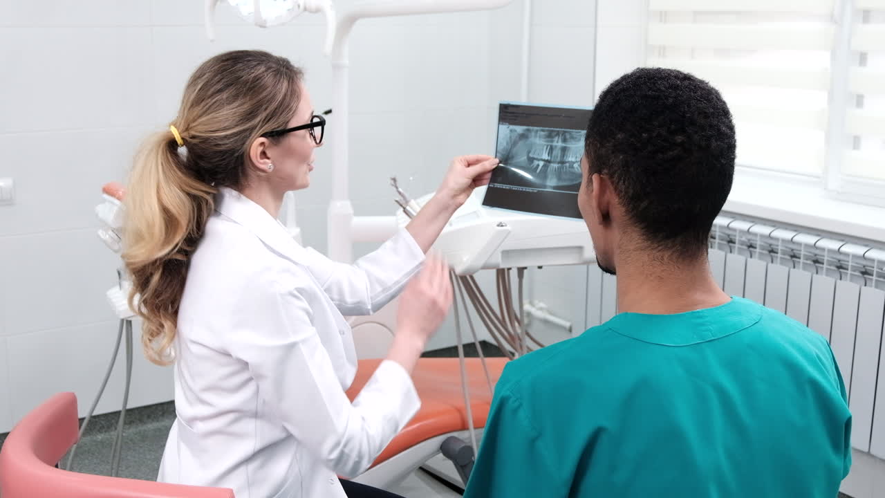 Dentista caucasiana explicando o raio-x para um(a) estudante. Equipamentos de consultório ao fundo