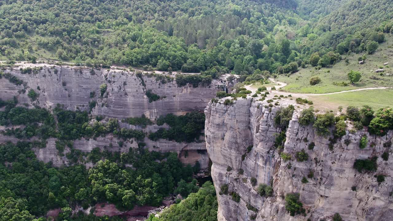 toma aérea de un acantilado alto pequeña cascada camino de tierra cerca de una zona boscosa densa montaña lateral