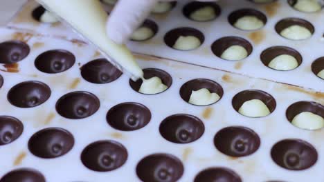 chocolatier pouring ganache filling into chocolate mold preparing candy
with a pastry bag