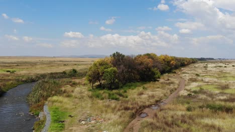 aerial drone shot of the river flowing under a remote gravel road bridge in the johannesburg, south africa