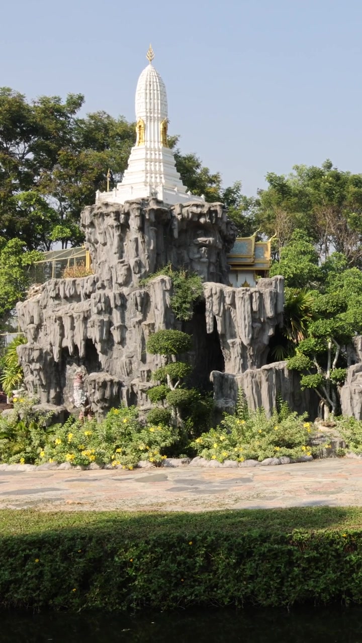 Ảnh chụp dọc thanh bình một ngôi tháp Phật giáo màu trắng trên khối đá nhân tạo và khu vườn