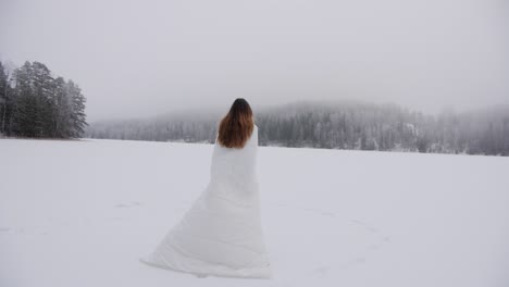 woman in white snowy outfit walking over a frozen lake in slow motion with a mist over forest in the background