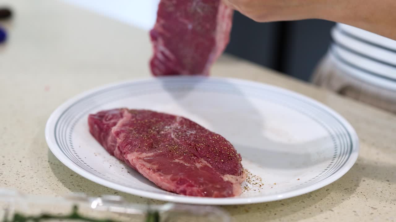 Hands seasoning beef steaks with salt and pepper on a plate in a bright kitchen setting