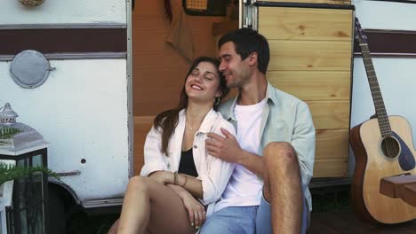 Lovely-portrait-of-a-young-couple.-They-are-sitting-on-the-stairs-of-their-modern-trailer,-embracing-and-smiling.-Dreaming-and-thoughtful-mood