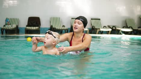 young mother is teaching her little cute son to swim in the swimming pool. she is holding his hands and playing in the water